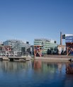 Four buildings covered with glass windows placed right beside each other very close to the habour. They each have a crane-like structure in the front. That means - poles geometrically structured across each other for a strong hold.