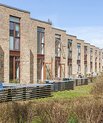 A row of modern, brown-brick terrace houses with small front gardens in daylight.