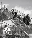 People walking down stairs at the trainstation, they have luggage with them. Black and white.
