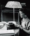 A young woman sitting by a desk writing on a typewriter