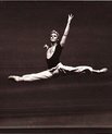 black and white picture of man leaping into the air with his left leg straight out behind him and his right straight out in front with upper body very straight and arms in a graceful ballet position