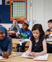 Primary school children of different ethnicities sitting in a classroom beside each other. Smiling, looking at the board.
